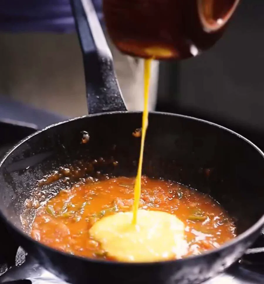 Beaten eggs being poured into a pan of simmering tomatoes and peppers