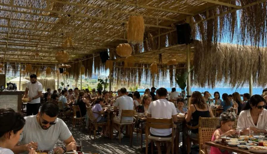 NANN's open terrace at Almare Beach: reed canopy, wicker lamps and the Aegean sea behind the tables